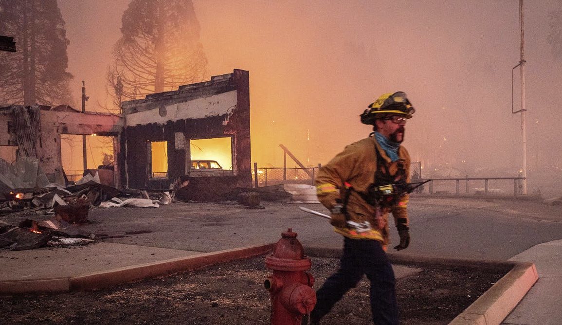 A photo of a firefighter walking through a burnt out environment.
