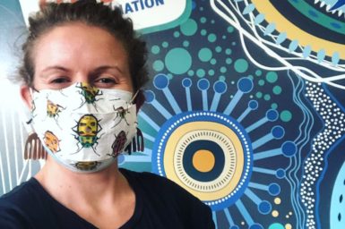 Woman with insect mask on smiling in CSIRO shirt. Showing of Music you can get vaccinated to