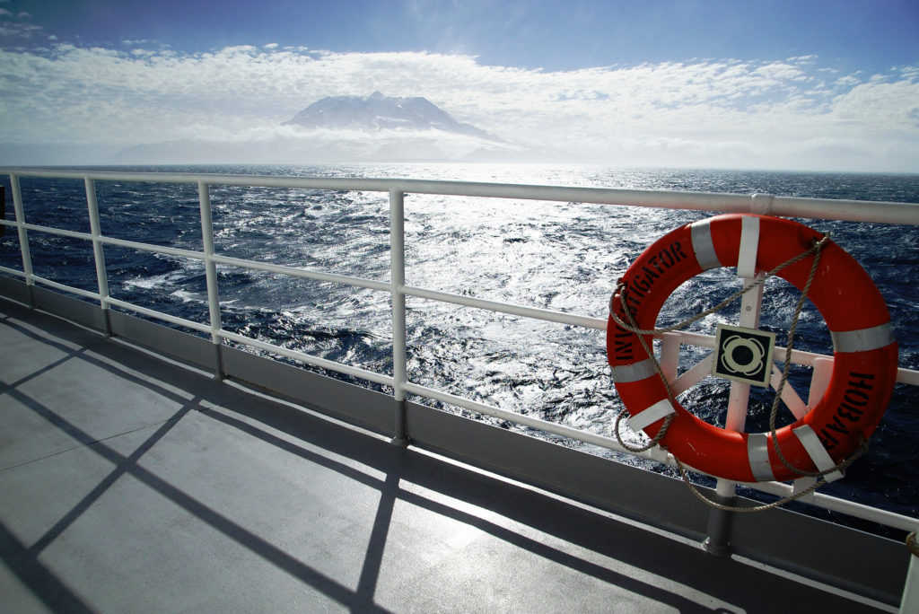 A view across the deck of a ship to an offshore island surrounded by cloud.