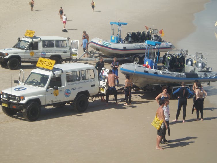 Two 4WD vehicles on the beach towing diving boats.