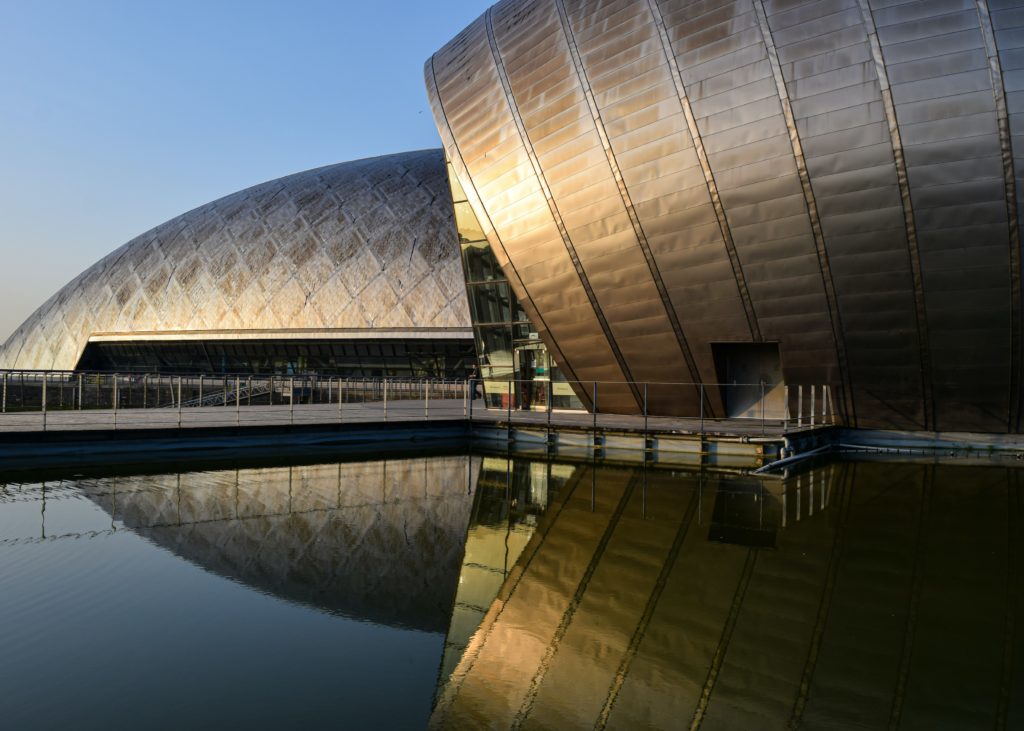 A curved dome building in front of water with a reflection.