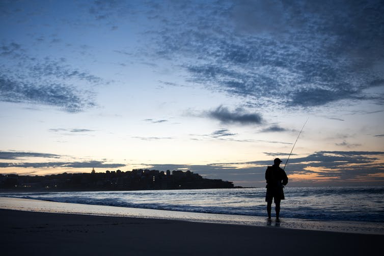 A person is fishing into the ocean from the sand.