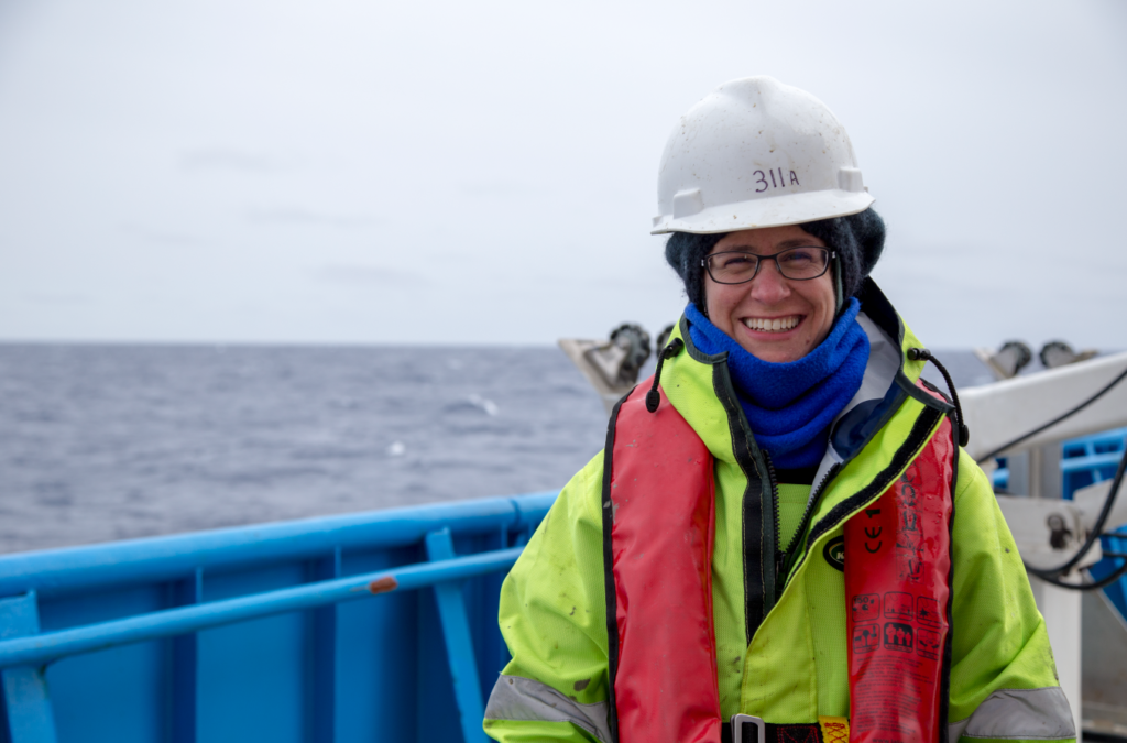 A scientist in hard hat and life preserver on the deck of a ship on the ocean.