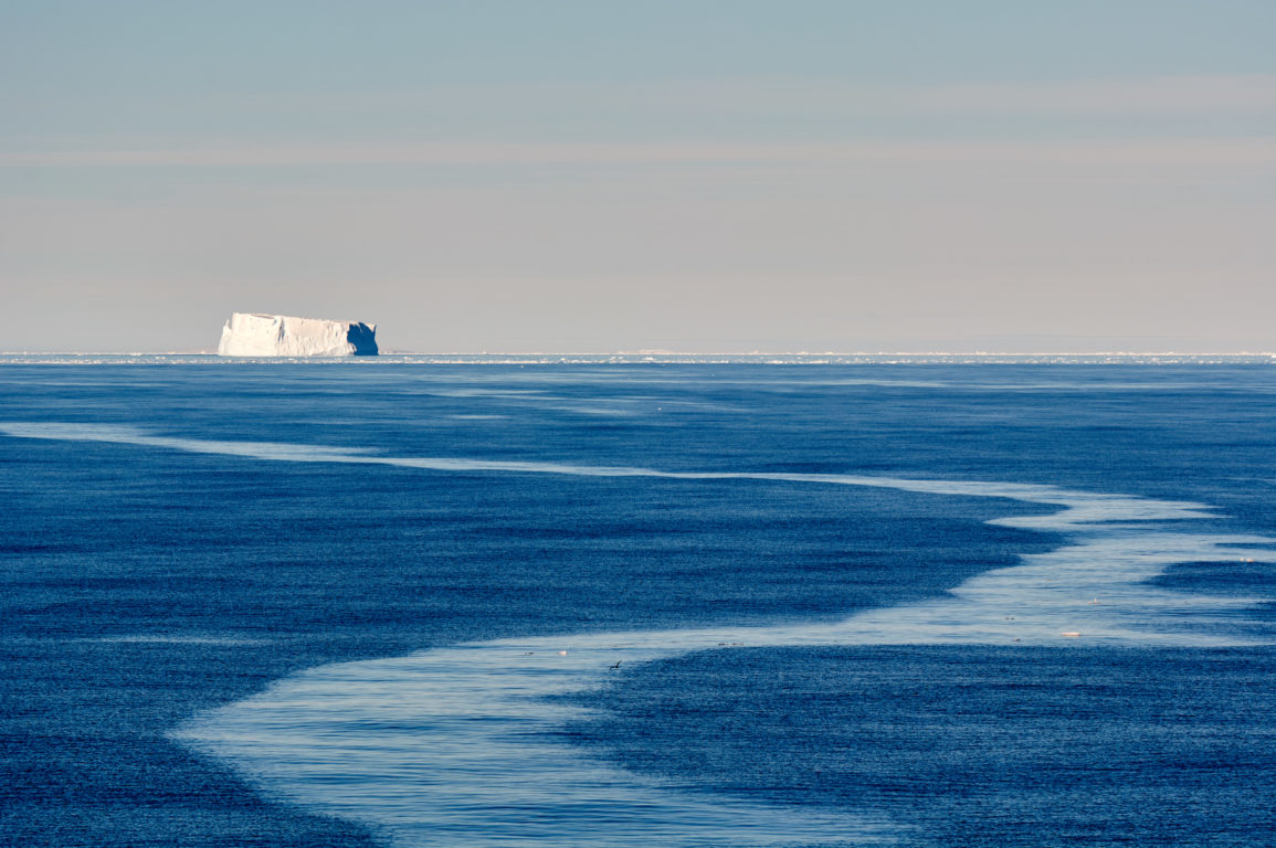 An iceberg on the horizon with a calm ocean in the foreground.