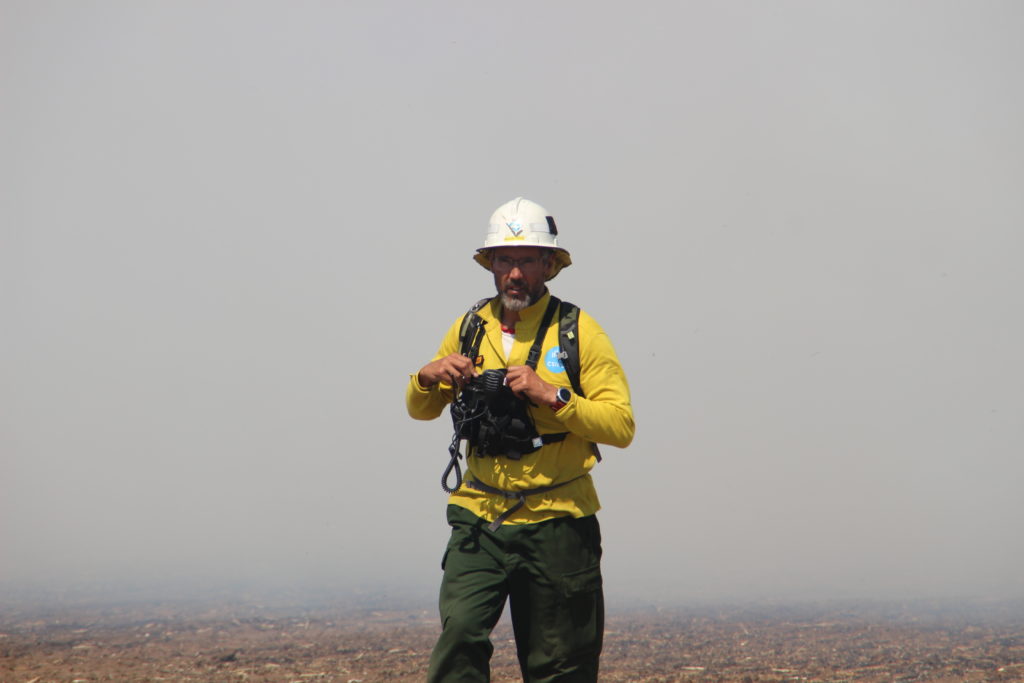 Dr Miguel Cruz in a hard helmet with a black bag in a smokey field. 