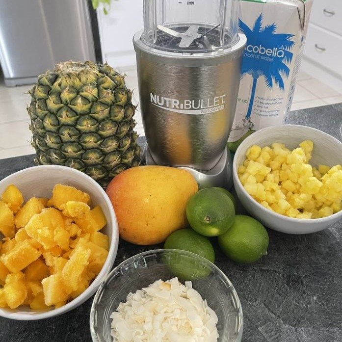 a table of ingredients for a refreshing mango splice drink including mango, lime, pineapple and coconut