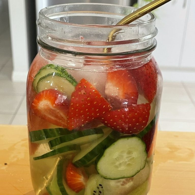 a jar style cup full of water with chopped berries and cucumber