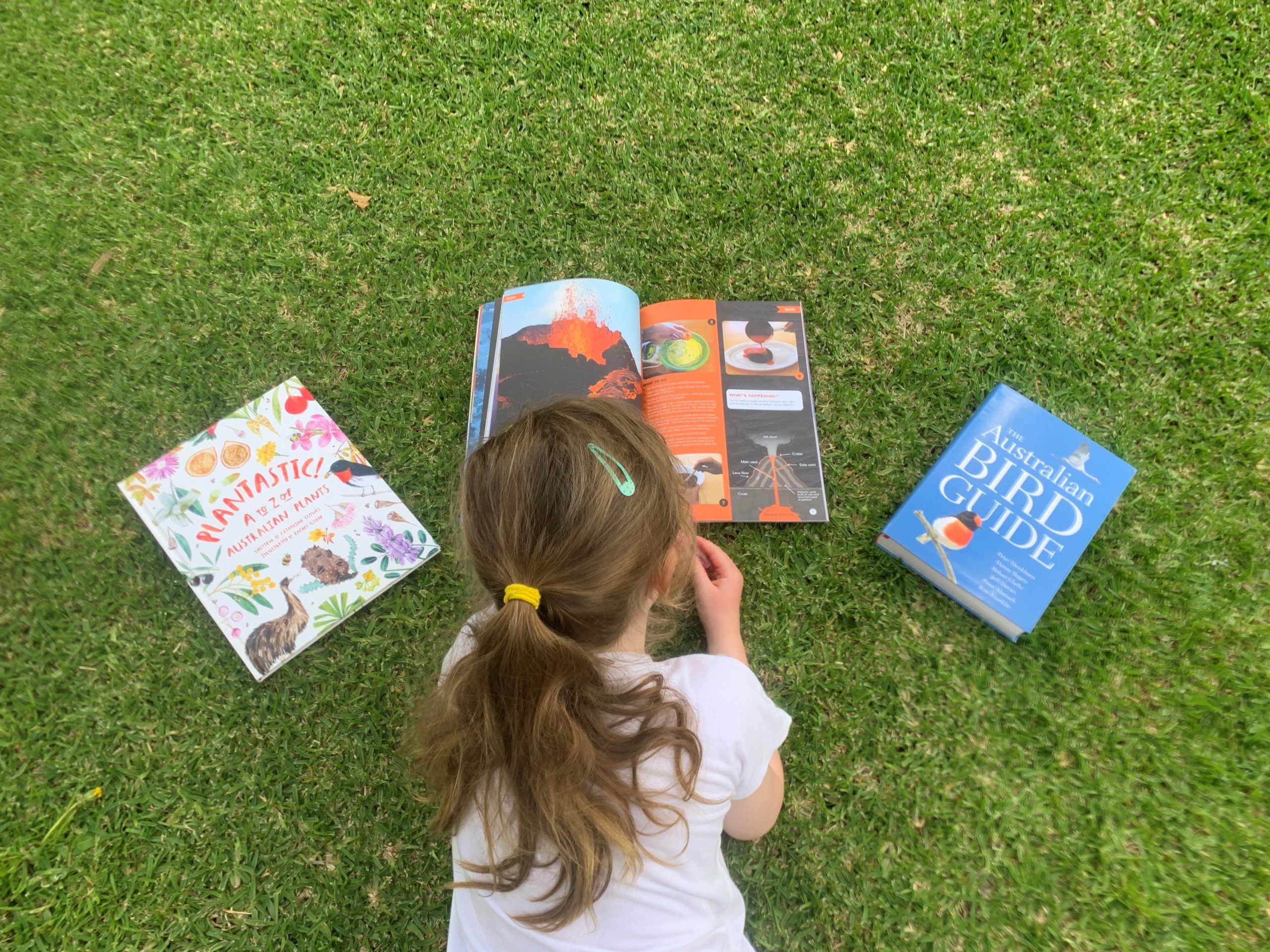 young child lying on the grass reading books