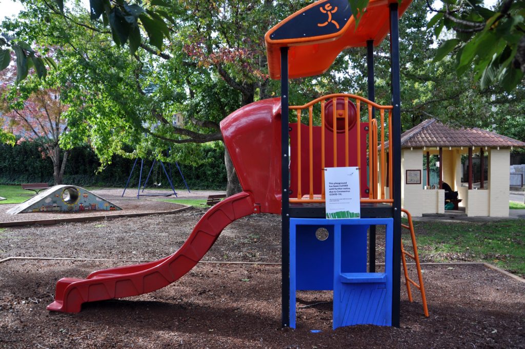 Nature Nurture Outdoors. An orange and red climbing frame with a slide. There is a paper sign attached to the climbing frame that says the park is closed due to COVID. 