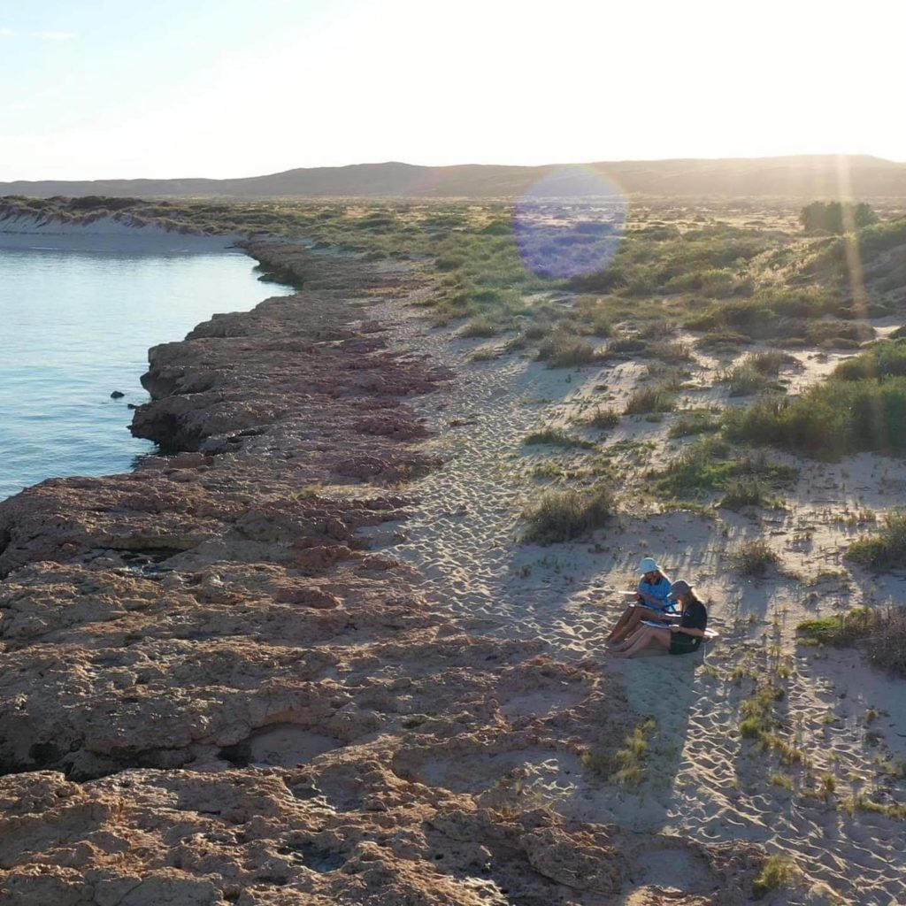 Two researchers walk along a rocky cliff/beach at Ningaloo Reef.