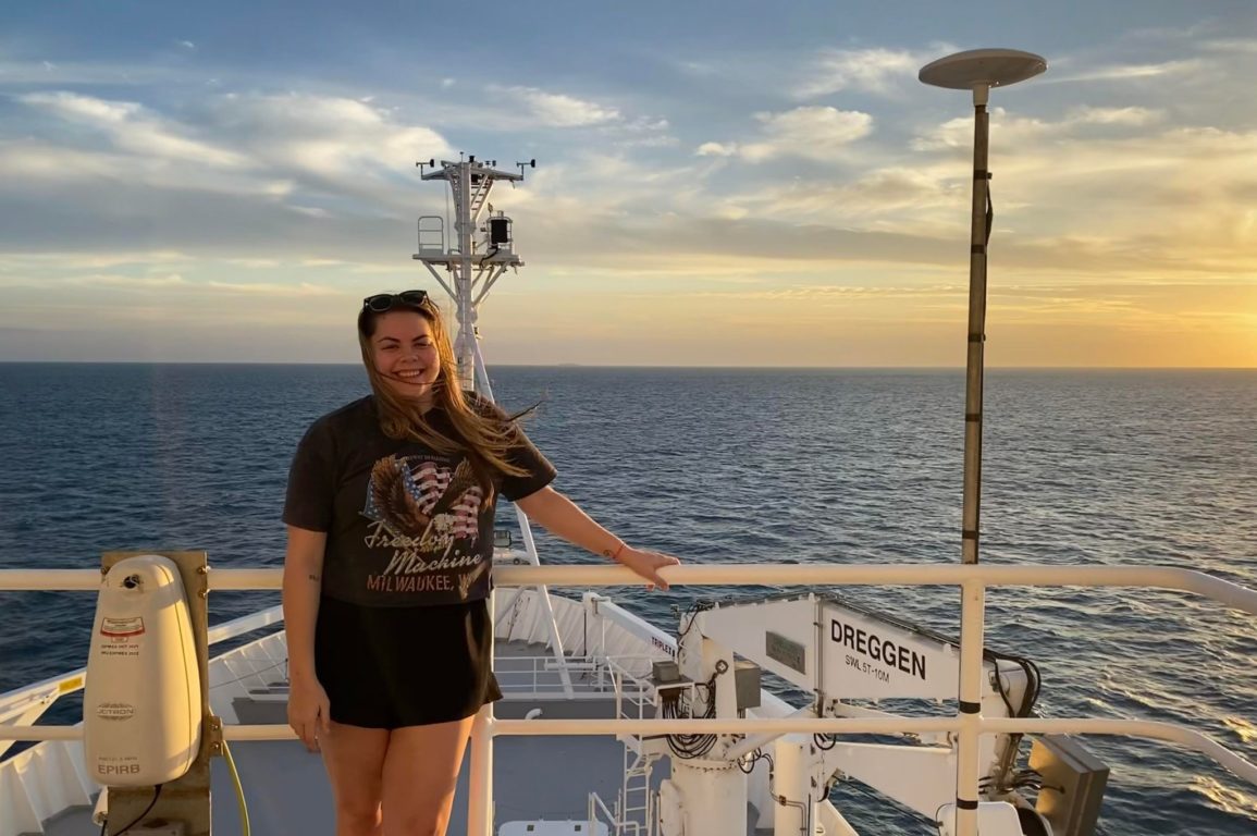 A photo of Hannah McCleary standing on a ship with the ocean in the background.