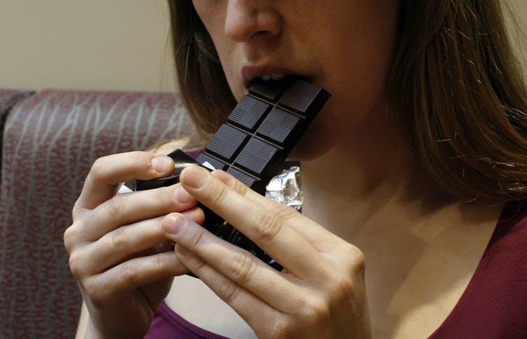 Women taking a bite from the corner of a block of chocolate. Nutritional food swaps.