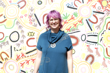 Nina Welti is standing in front of a colourful wall