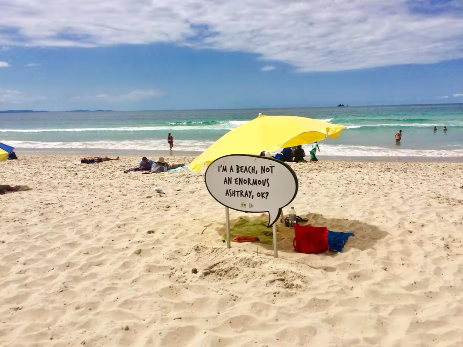 A photo of a beach with a sign in the sand reading "I'm a beach, not an enormous ashtray, ok?"