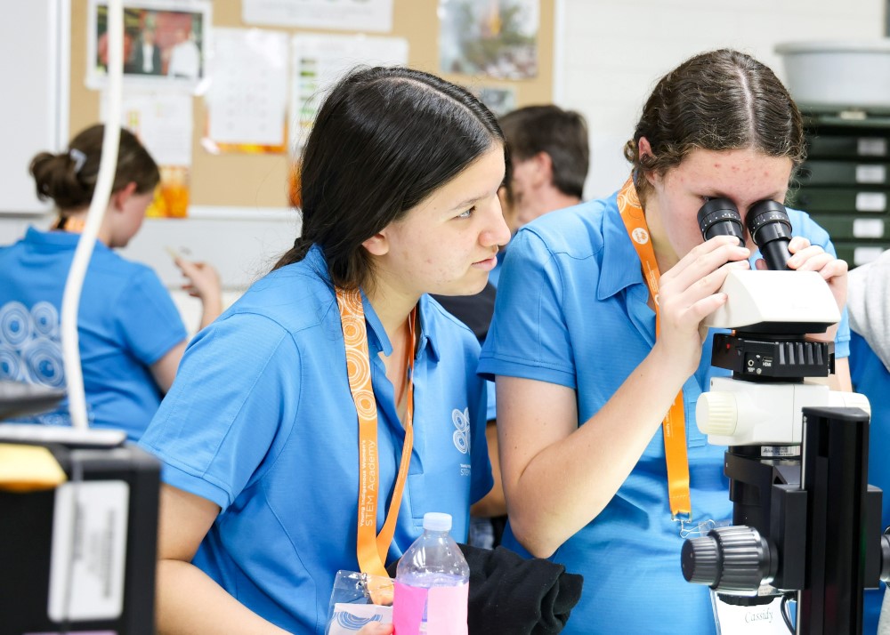 Young Indigenous Women's STEM Academy students in blue polos using a microscope