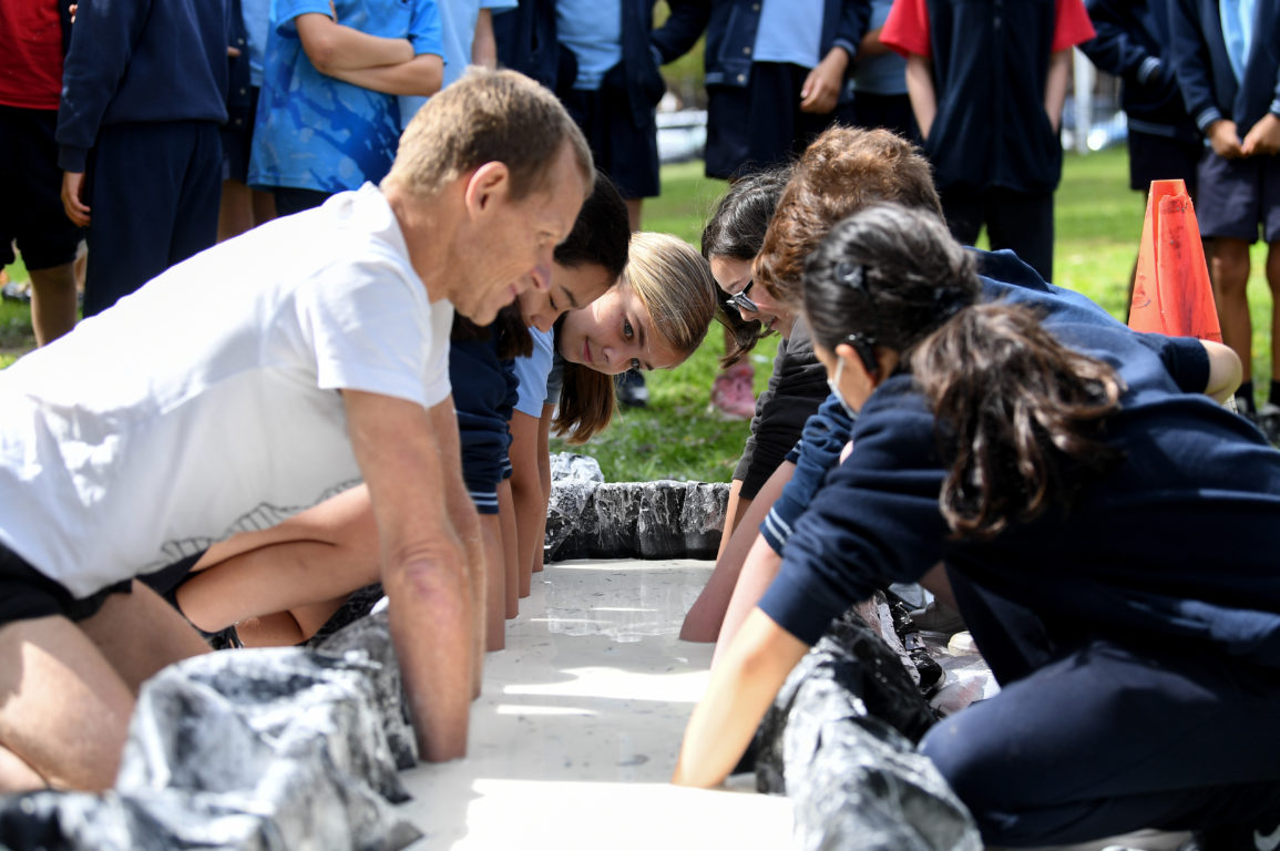 An adult and a group of children surround a large trough. Their hands are immersed in the thick, white liquid.