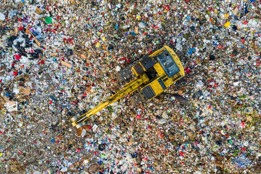 Birds eye view of a dump filled with waste. There is a digger on top.