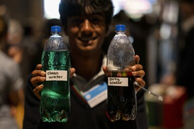 A student holding out two bottles of coloured liquid, one is labelled 'clean water', the other is labelled 'dirty water'.