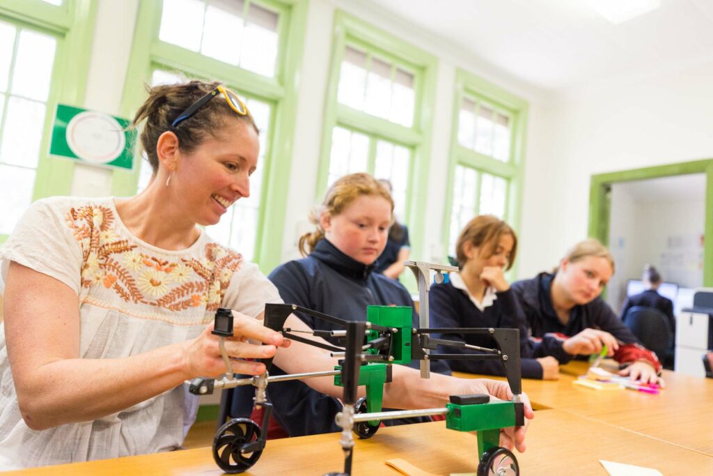 A female teacher working on a plastic model alongside three primary school students at a desk