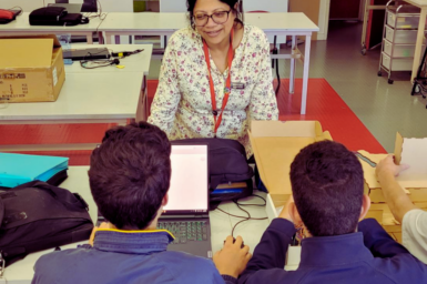 Veena, a middle aged woman leans over a desk while teaching two male students