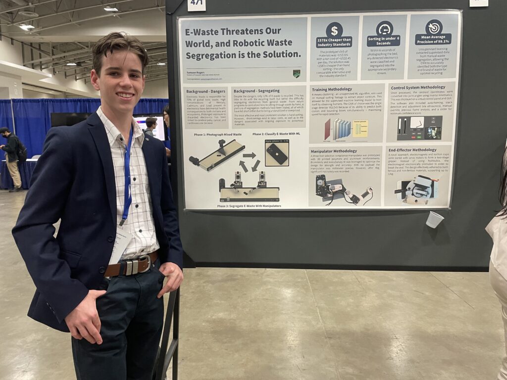 Samson Rogers wearing a suit at the AAAI conference. Sam stands in front of a poster for his project and smiles at the camera